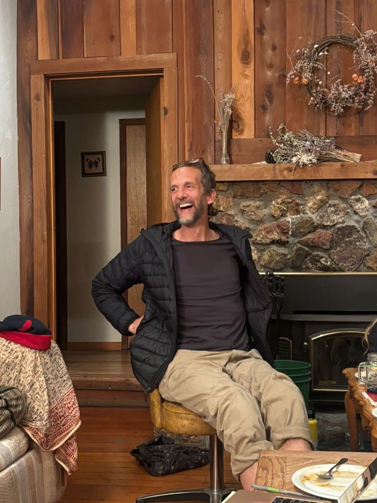 A camper laughing by the fireplace in the retreat's wood-paneled common room