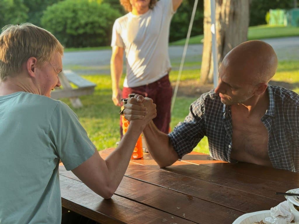 Two campers arm wrestling at a picnic table at golden hour