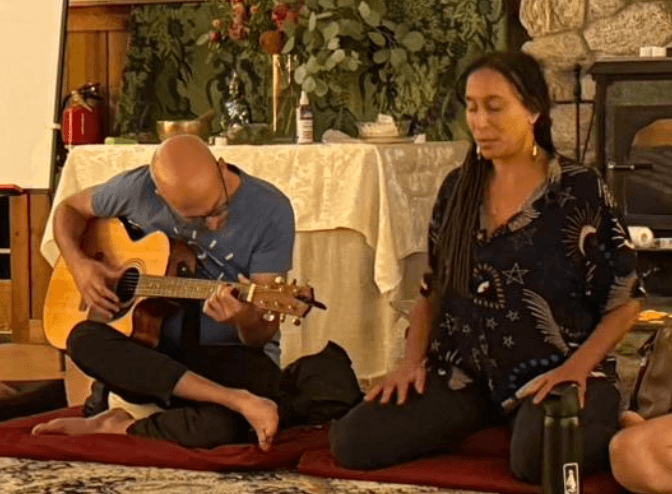 A facilitator playing guitar beside another leading a grounding song